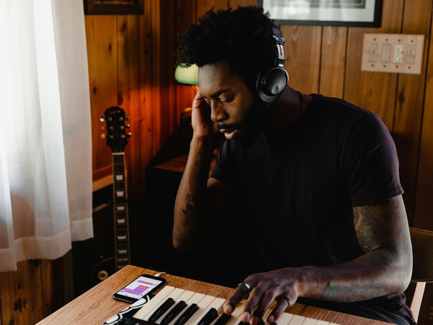 A musician in a home studio wearing headphones and working at a MIDI keyboard