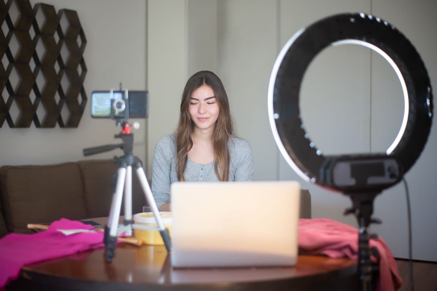A creator filming at a table with a ring light, phone on a tripod and a laptop